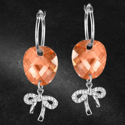 Brandy Bow Earrings featuring sterling silver hoops with faceted peach-colored stones and sparkling bow-shaped charms, designed for women’s elegant jewelry collections.