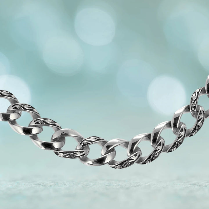 Close-up of a male stainless steel Enigma Steel Necklace featuring polished and textured interlocking links against a soft blue blurred background.