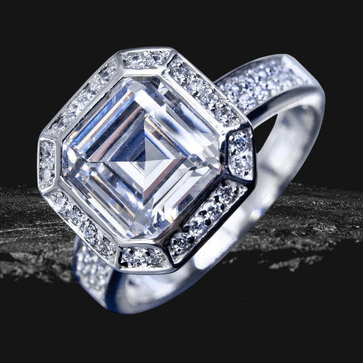 Asscher Deco Ring featuring a large square-cut center stone surrounded by smaller stones, set in sterling silver with rhodium plating for a polished, elegant look.
