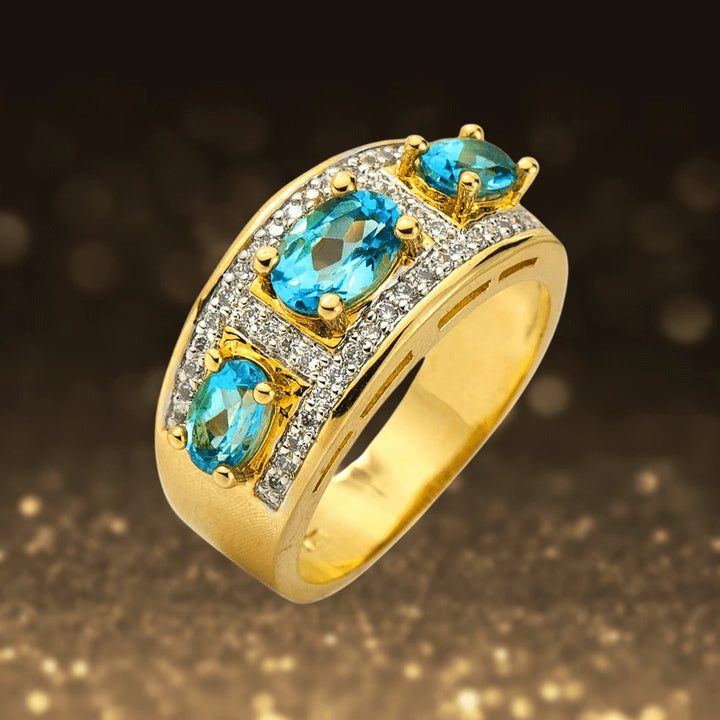 Mayfair Ring featuring sterling silver with gold plating, adorned with three vibrant blue gemstones and a row of sparkling clear crystals for an elegant jewelry statement.