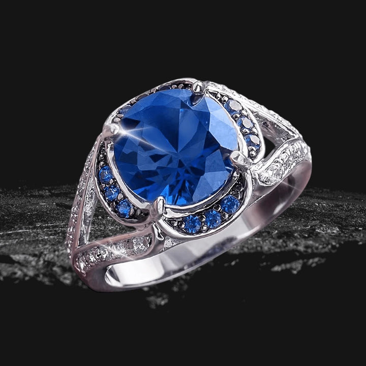 Electra Ring featuring a large blue gemstone set in sterling silver with rhodium plating, surrounded by smaller blue and white stones, designed for women’s jewelry.