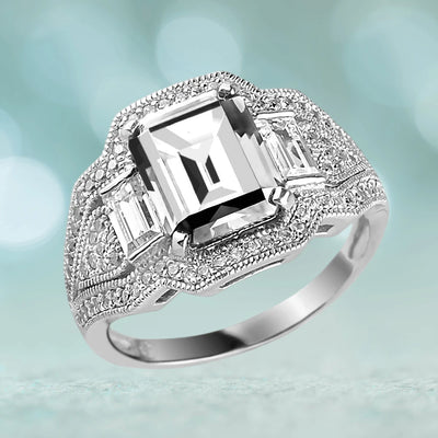 The Elizabeth Ring featuring a sterling silver band with rhodium plating, showcasing a large emerald-cut clear gemstone surrounded by smaller sparkling stones, designed for women.