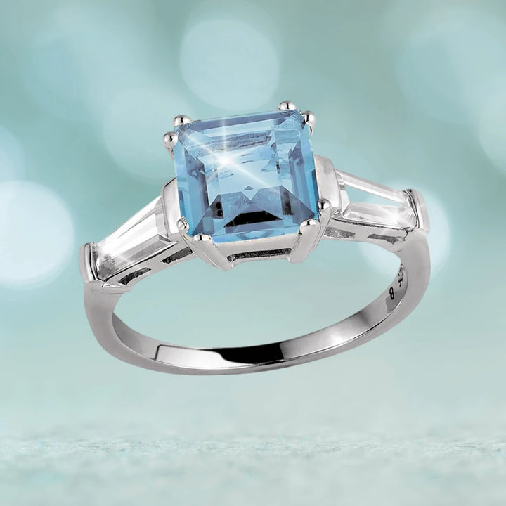Decadence Gem Ring Blue Topaz featuring a square blue topaz center stone set in sterling silver with rhodium plating, designed for a female jewelry collection.