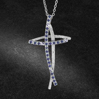 Decoria Rhodium Cross Pendant featuring a delicate rhodium plating with blue gemstone accents on a feminine chain necklace against a dark background.