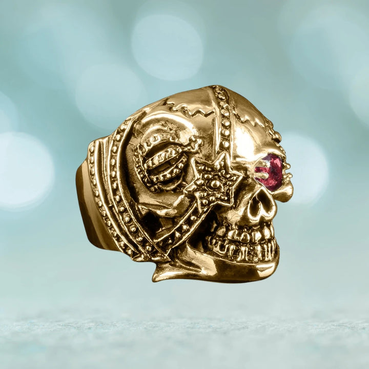 Riotous Skull Ring crafted in gold-plated stainless steel featuring a detailed skull design with a red gemstone eye, a bold jewelry piece for male fashion.