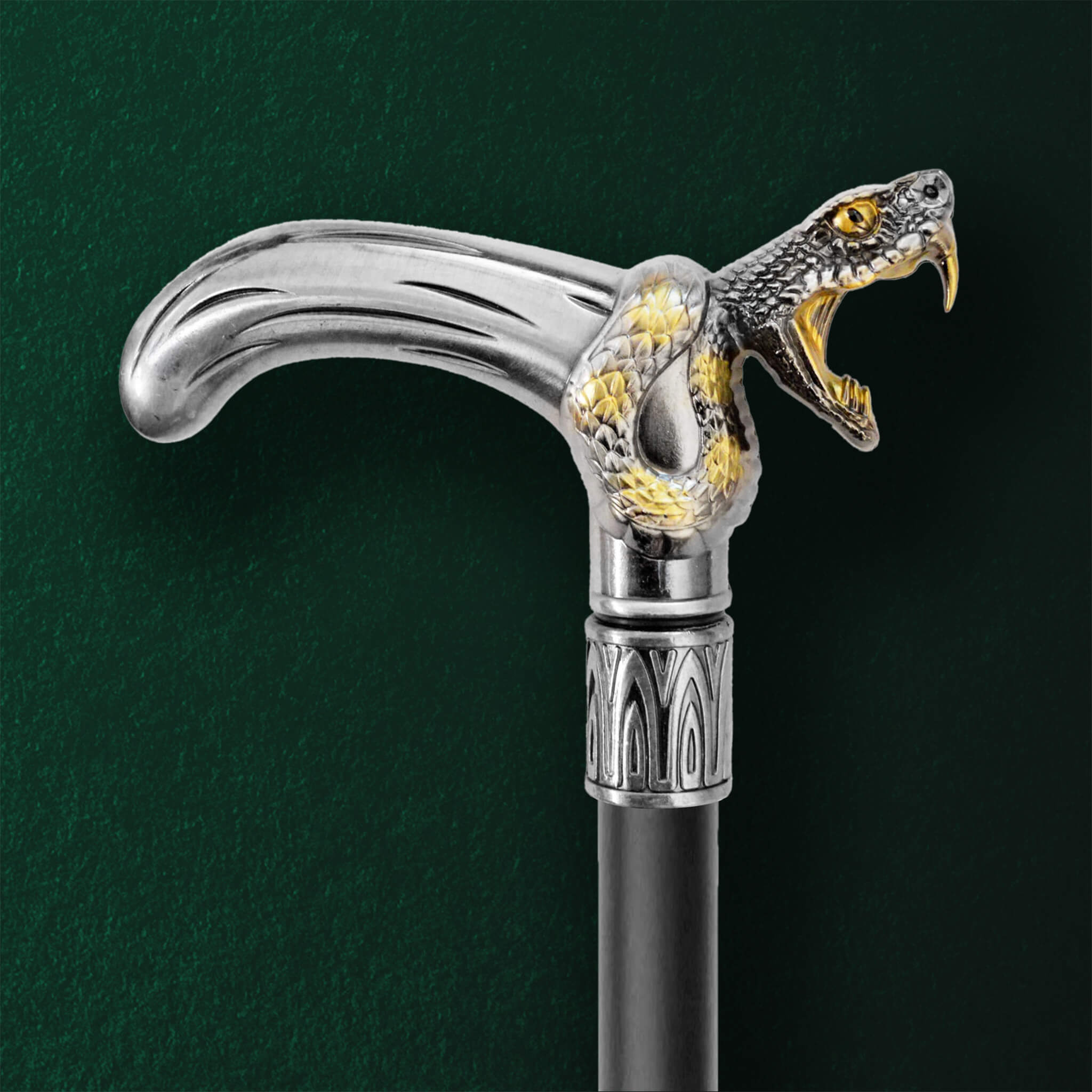 Close-up of a Black Fang Walking Cane handle featuring a detailed silver snake design with gold accents and fangs wrapped around the curved grip against a dark green background.