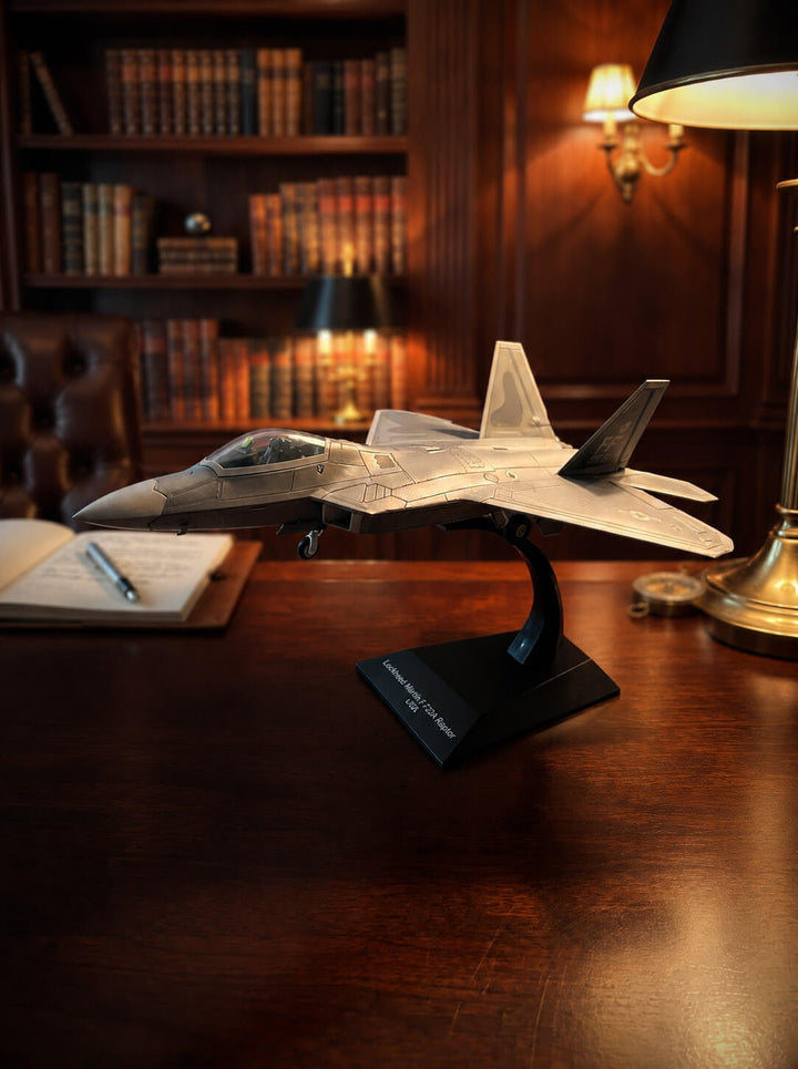 F-22A Raptor model fighter jet on a display stand atop a wooden desk in a warmly lit library setting. Up To 75% Off Retail