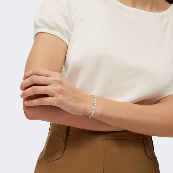 Female model wearing a Millionaire Gold Tennis Bracelet made of sterling silver with gold plating, styled with a white top and brown pants, showcasing elegant jewelry.