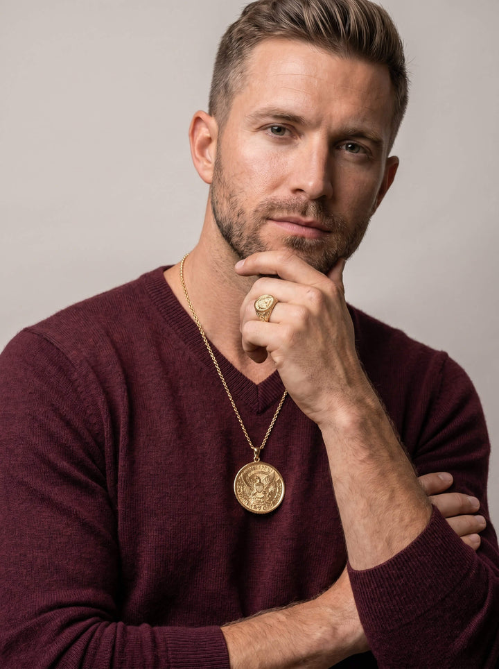 Man wearing a gold pendant necklace and matching ring with an eagle emblem, styled with a burgundy sweater, showcasing the American Glory Collection jewelry set.
