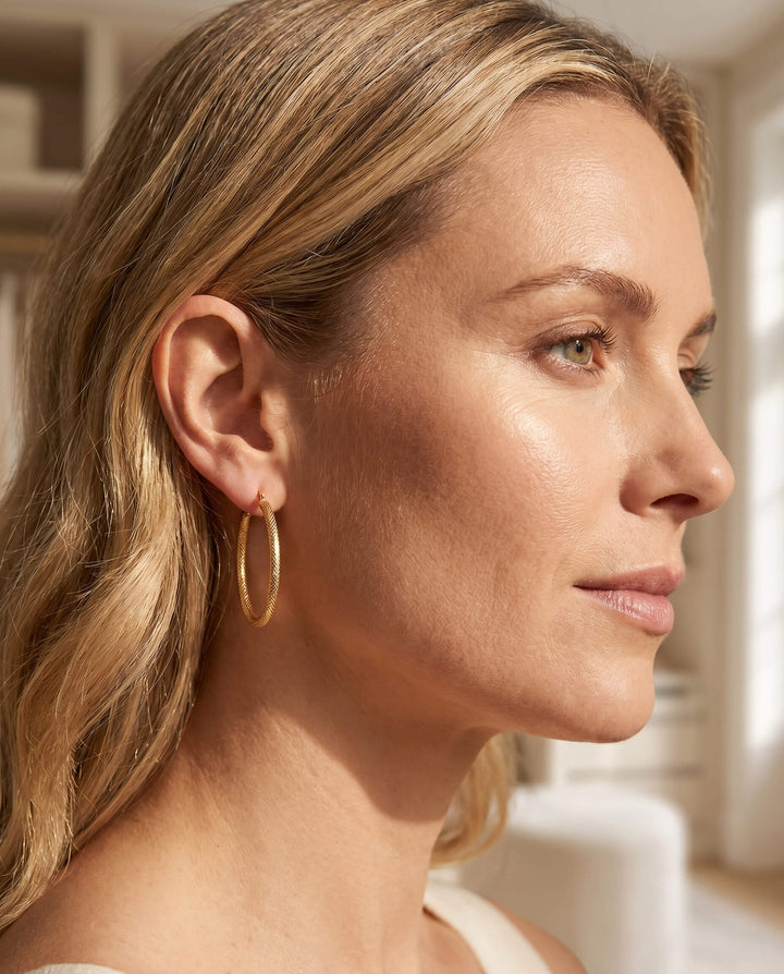Close-up of a woman wearing gold Lucente Hoop Oval Earrings, showcasing elegant and textured hoop design perfect for stylish jewelry collection.