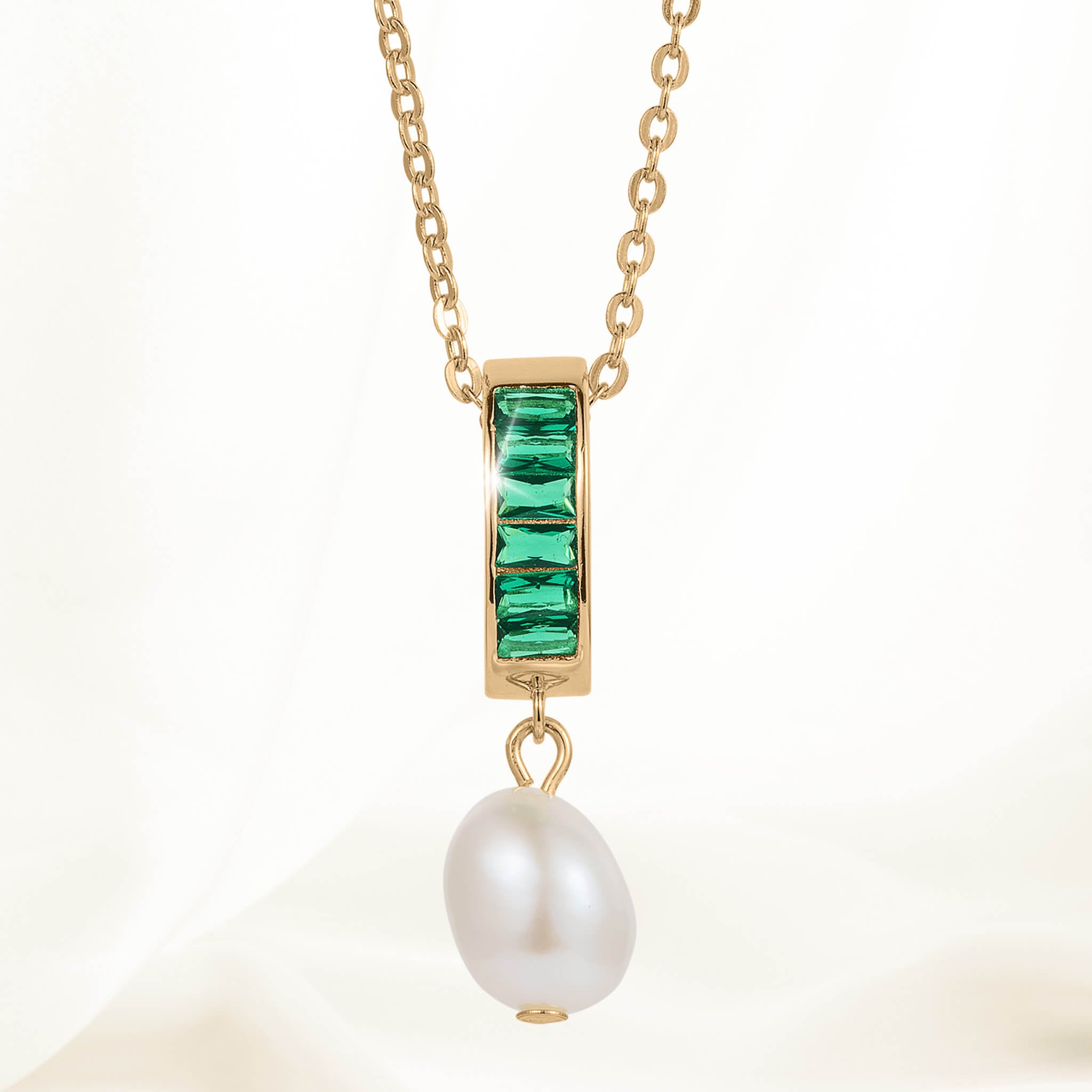 Pearl Radiance Pendant featuring a gold chain with a rectangular gold setting adorned with four green gemstones and a single white pearl drop pendant.