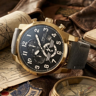 Airforce Gold Watch featuring a gold-tone case, black dial with white numerals, chronograph subdials, and a gray leather strap, styled with vintage aviator accessories. Up To 75% Off Retail.