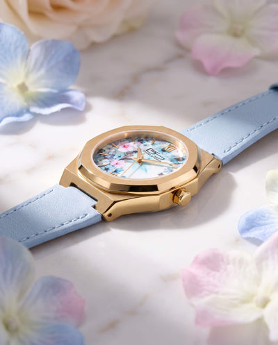 Fleur De Vie Ladies Watch featuring a gold tone case floral dial and light blue strap displayed among soft pastel flowers for an elegant jewelry look